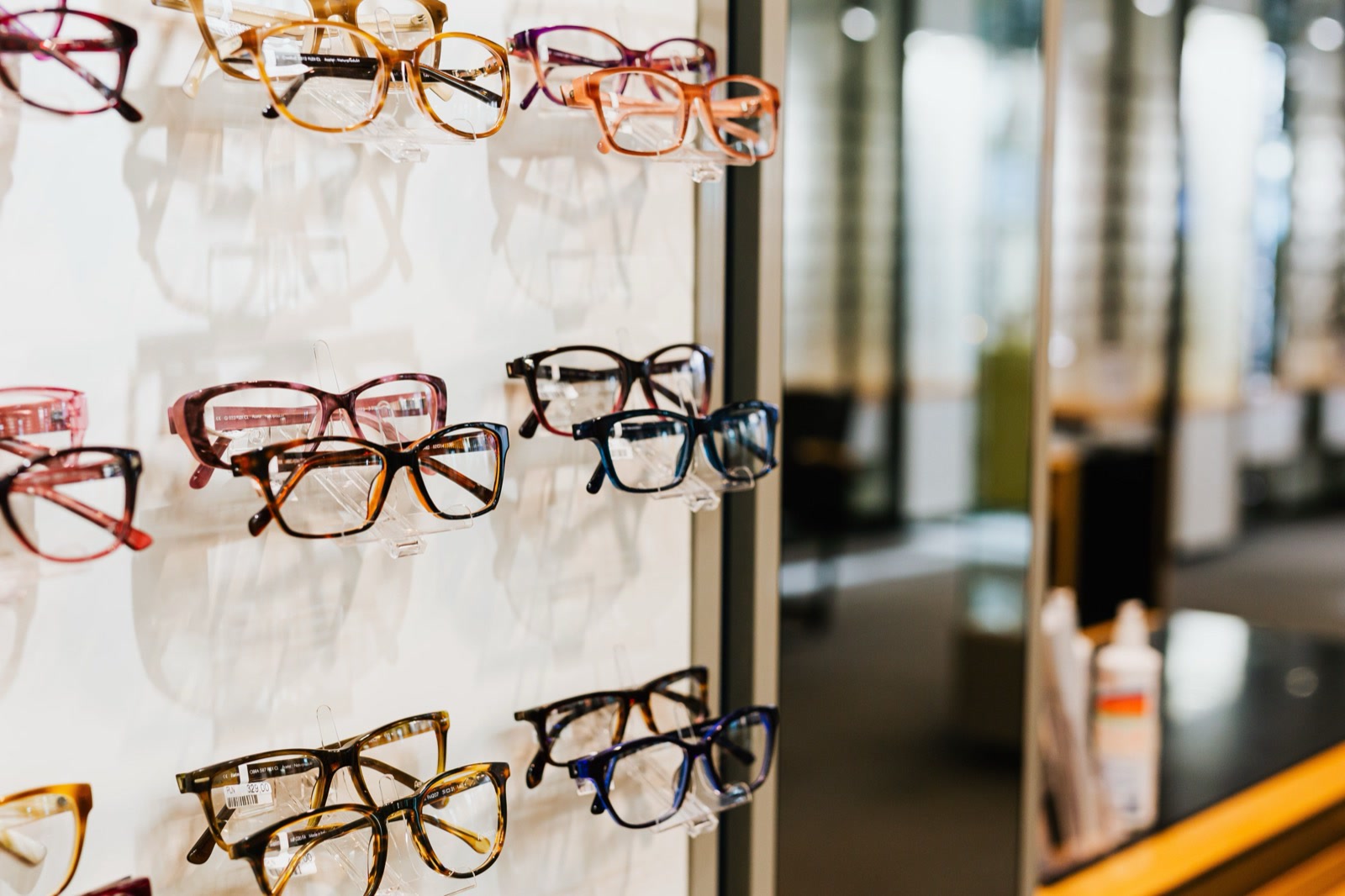 Spectacle frames in tortoiseshell, pink and blue on a lit wall display in an optical shop