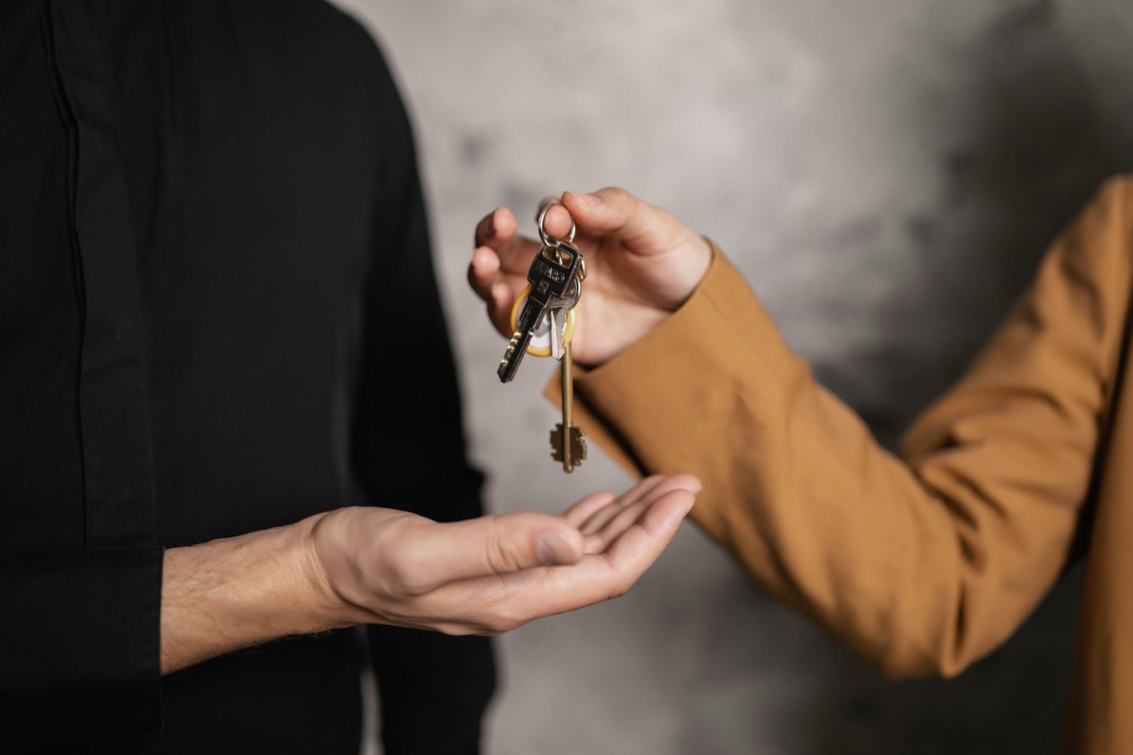 One person handing a bunch of keys to another, against a grey wall